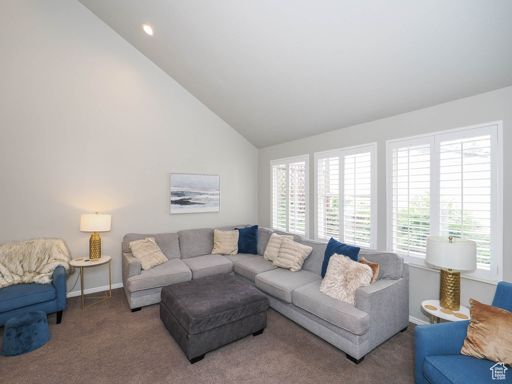 Living room with plenty of natural light, dark colored carpet, and high vaulted ceiling