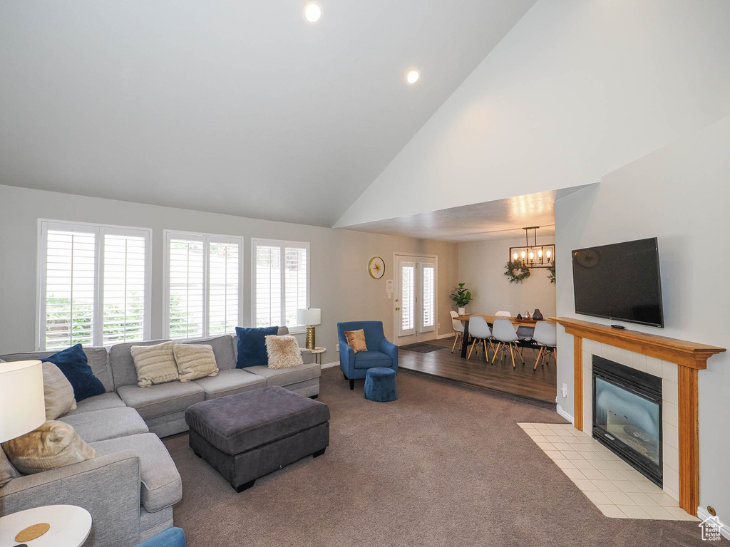 Carpeted living room featuring high vaulted ceiling, a tiled fireplace, and a chandelier