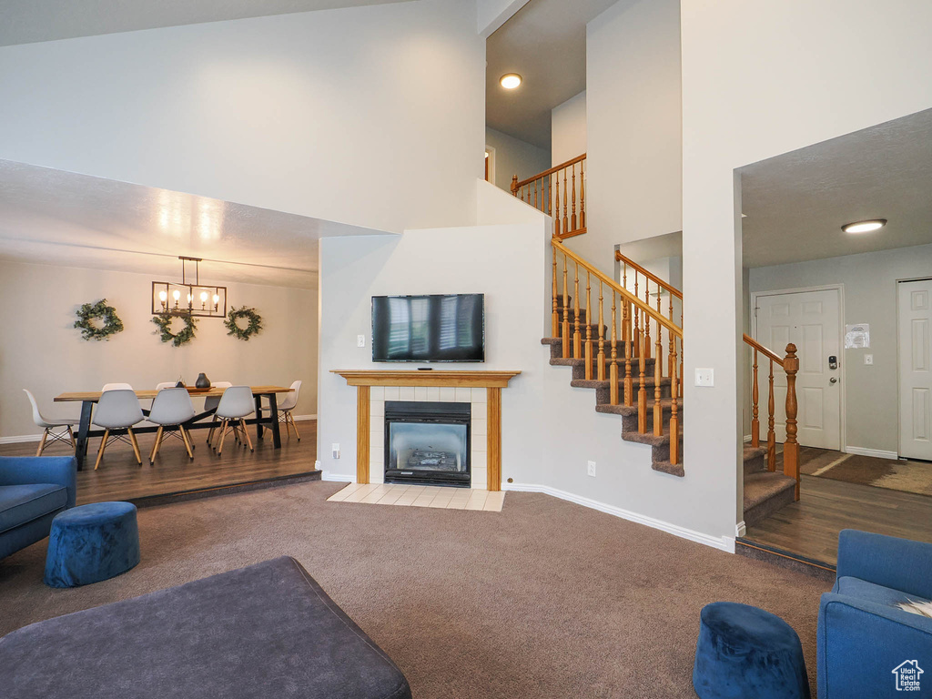 Carpeted living room featuring a notable chandelier, a towering ceiling, and a fireplace