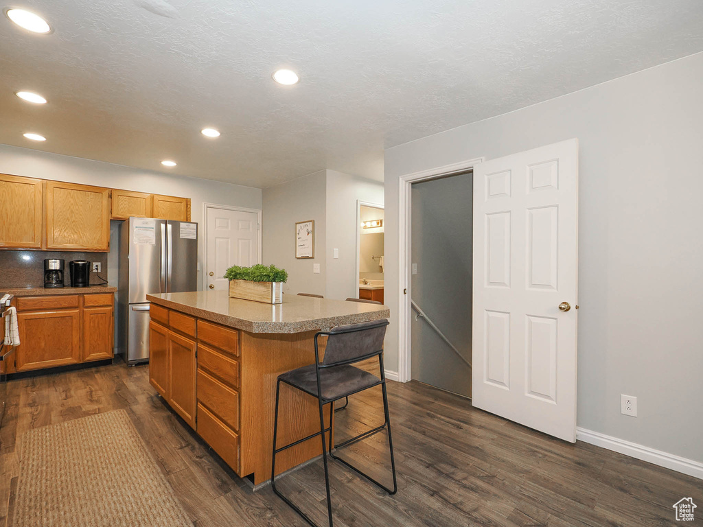 Kitchen featuring dark hardwood / wood-style floors, a kitchen breakfast bar, stainless steel fridge, tasteful backsplash, and a center island