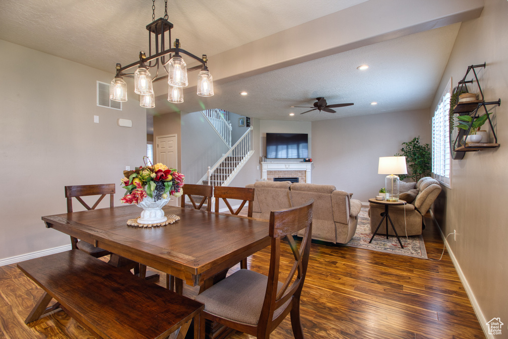 Dining room featuring ceiling fan, a fireplace, beam ceiling, and dark wood-type flooring