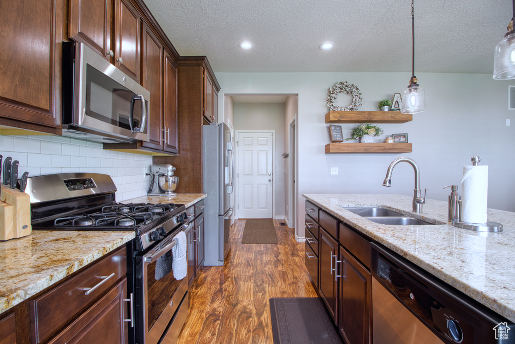 Kitchen featuring stainless steel appliances, dark hardwood / wood-style floors, decorative light fixtures, sink, and tasteful backsplash