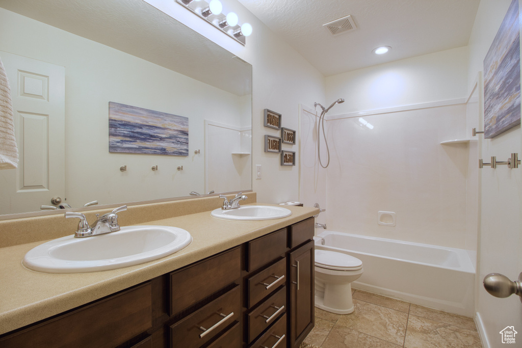 Full bathroom with tile flooring, double sink, bathing tub / shower combination, vanity with extensive cabinet space, and toilet