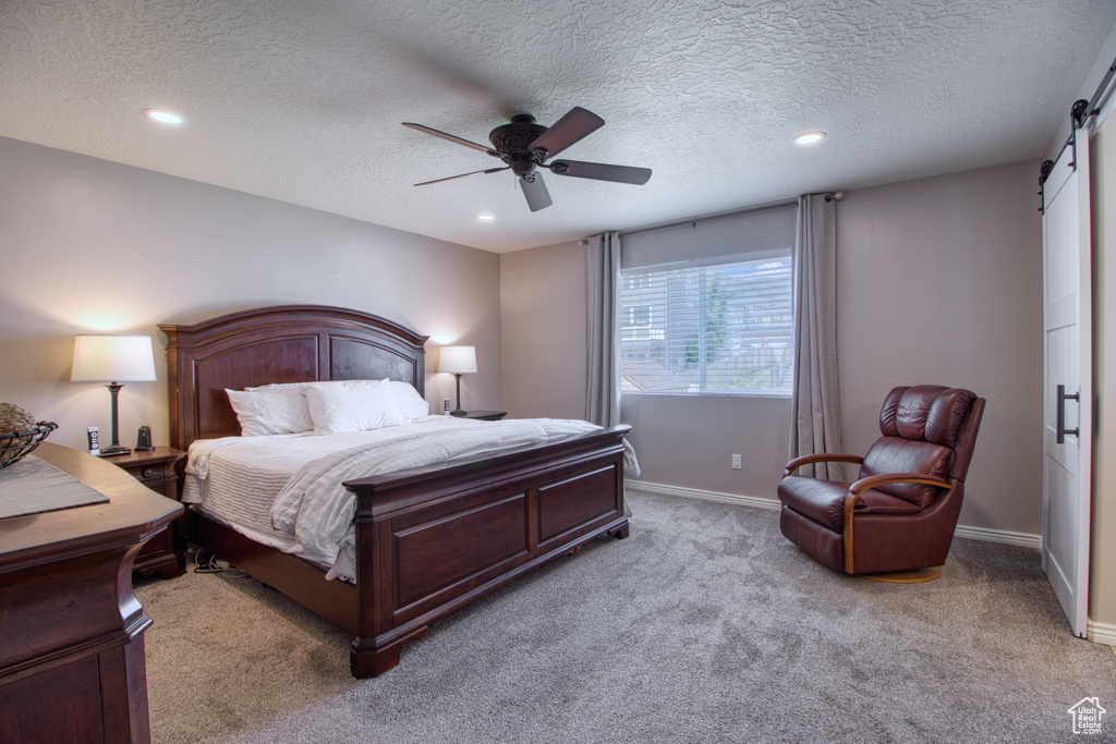 Bedroom with carpet flooring, a barn door, ceiling fan, and a textured ceiling