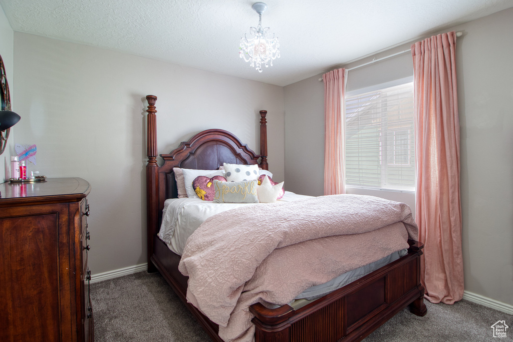 Bedroom featuring a notable chandelier, dark carpet, and a textured ceiling