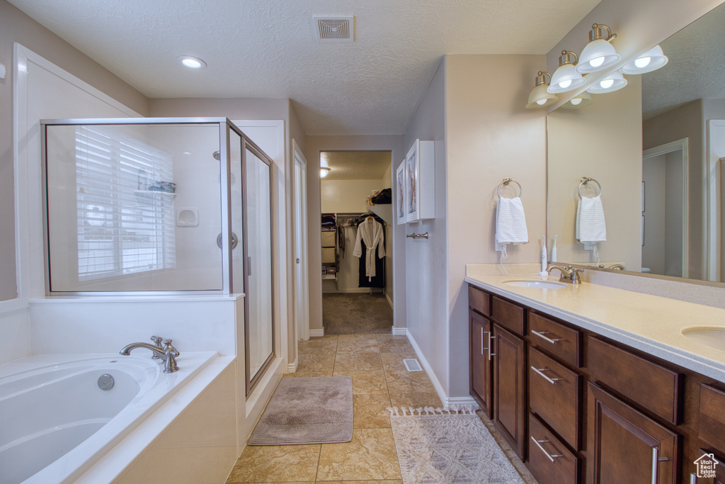 Bathroom featuring independent shower and bath, double sink vanity, tile floors, and a textured ceiling