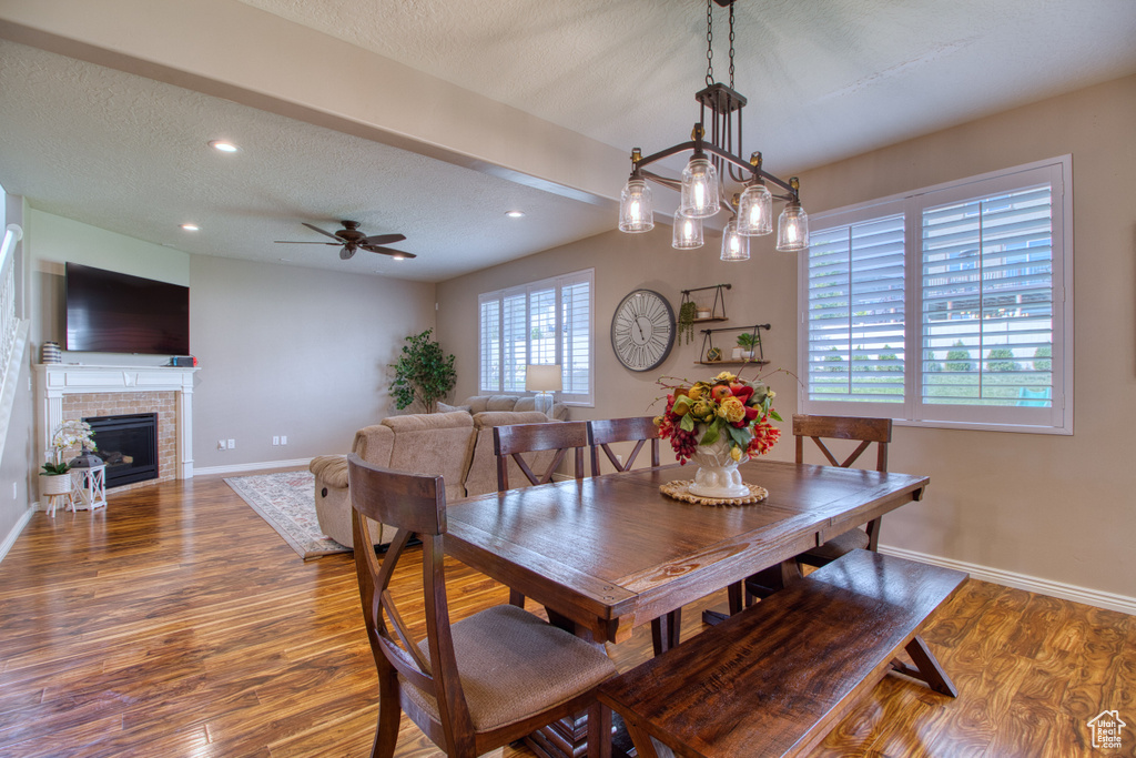 Dining room with a textured ceiling, a fireplace, wood-type flooring, and ceiling fan