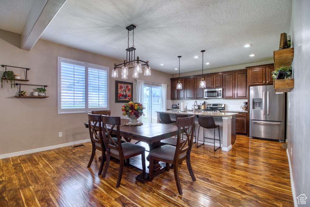 Dining room featuring a textured ceiling, dark wood-type flooring, beamed ceiling, a notable chandelier, and sink