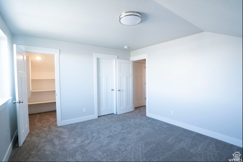 Unfurnished bedroom with a walk in closet, a closet, dark colored carpet, and vaulted ceiling