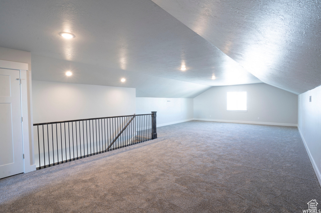 Additional living space with a textured ceiling, carpet flooring, and vaulted ceiling