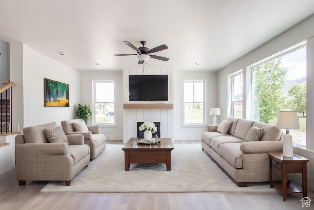 Living room with a large fireplace, light wood-type flooring, and ceiling fan