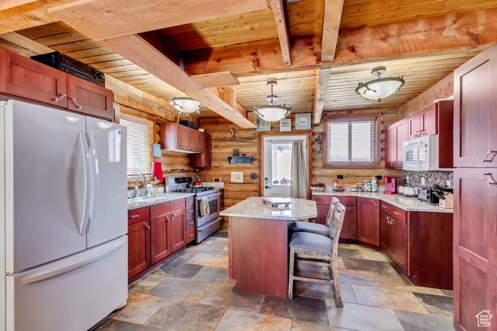 Kitchen with white appliances, sink, a center island, light stone countertops, and log walls