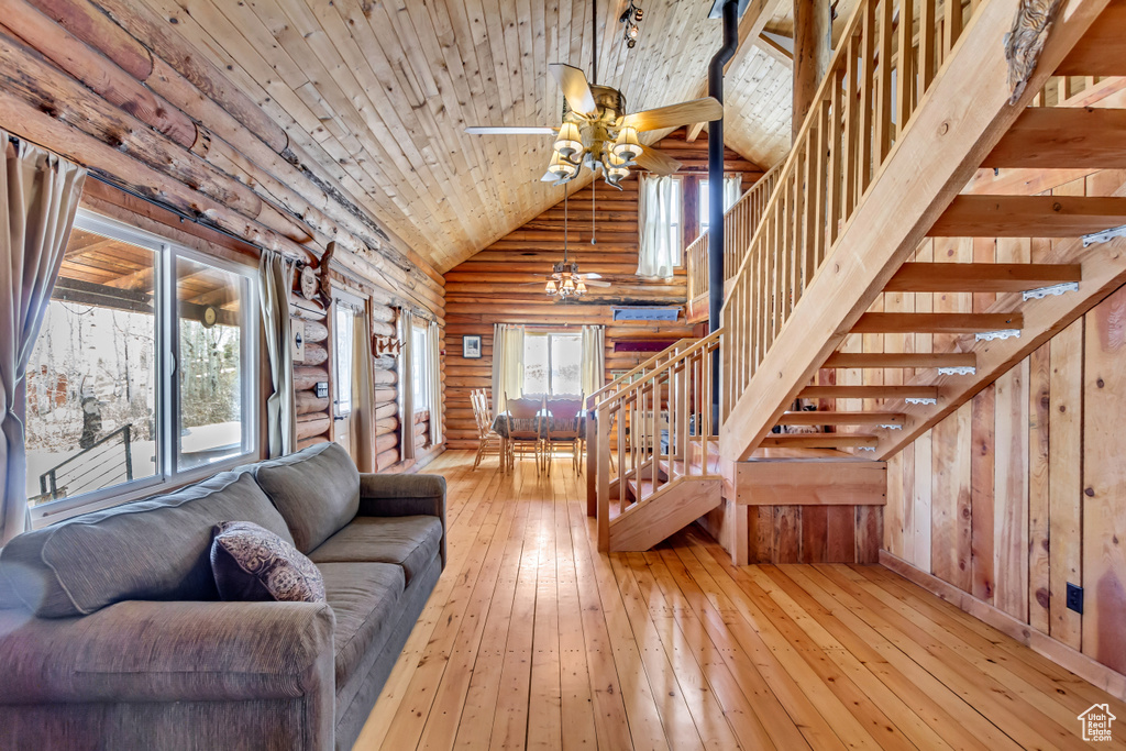 Living room with light wood-type flooring, log walls, ceiling fan, wooden ceiling, and high vaulted ceiling