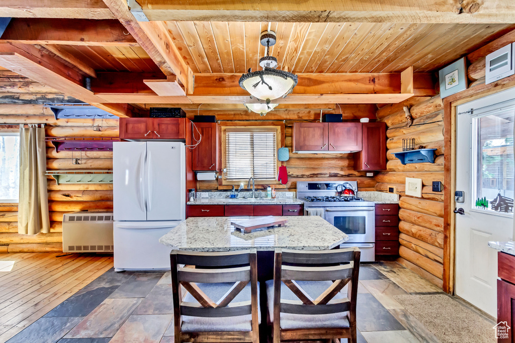 Kitchen featuring white fridge, double oven range, a wealth of natural light, and log walls