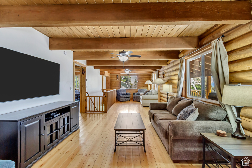 Living room with ceiling fan, wooden ceiling, light wood-type flooring, rustic walls, and beamed ceiling