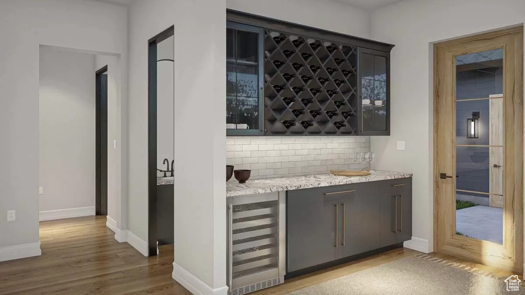 Bar with wine cooler, hardwood / wood-style floors, tasteful backsplash, and light stone countertops