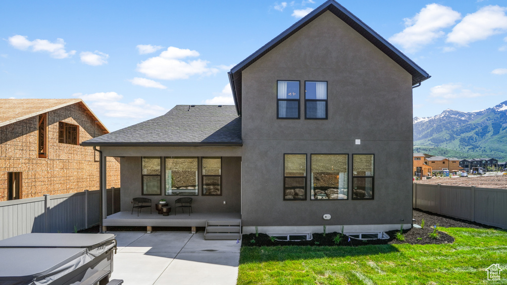 Rear view of house with a patio area, a lawn, and a mountain view