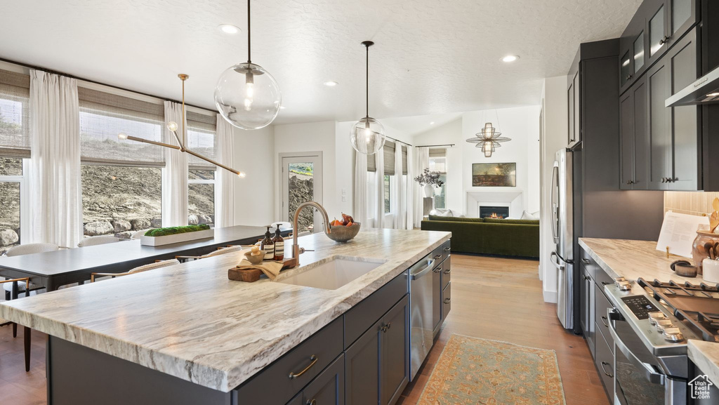 Kitchen featuring decorative light fixtures, light hardwood / wood-style floors, a center island with sink, sink, and appliances with stainless steel finishes