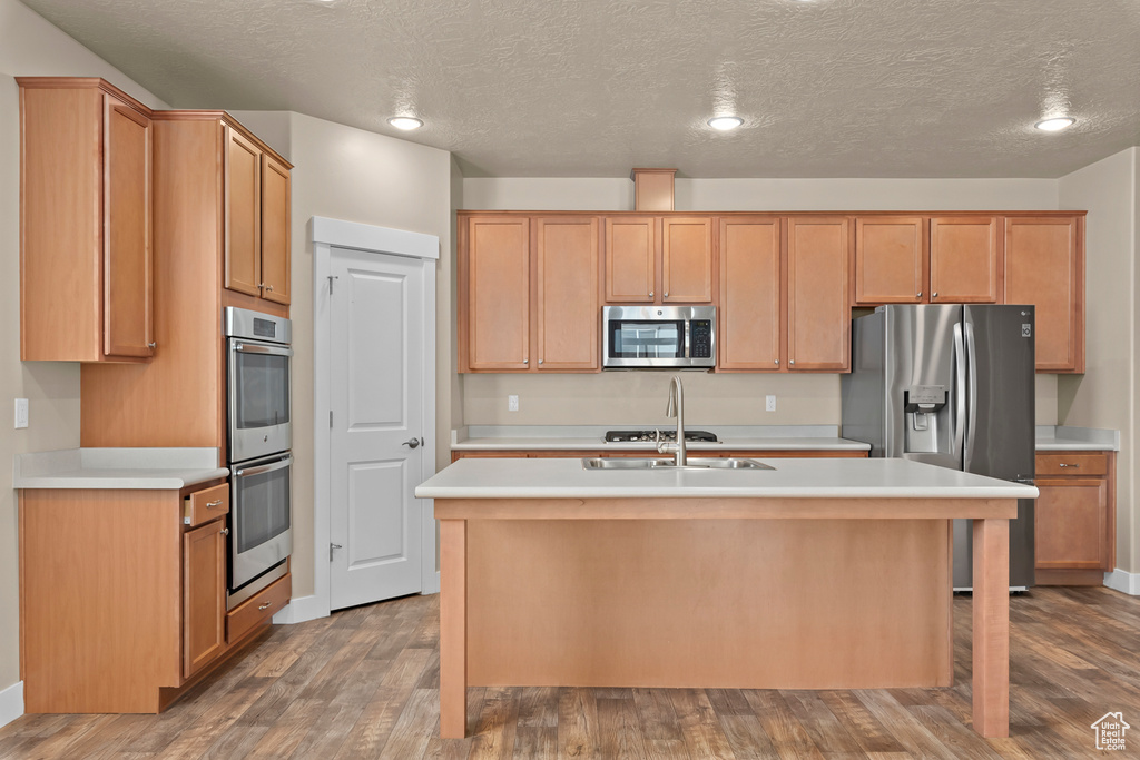 Kitchen featuring a center island with sink, a textured ceiling, hardwood / wood-style flooring, and appliances with stainless steel finishes