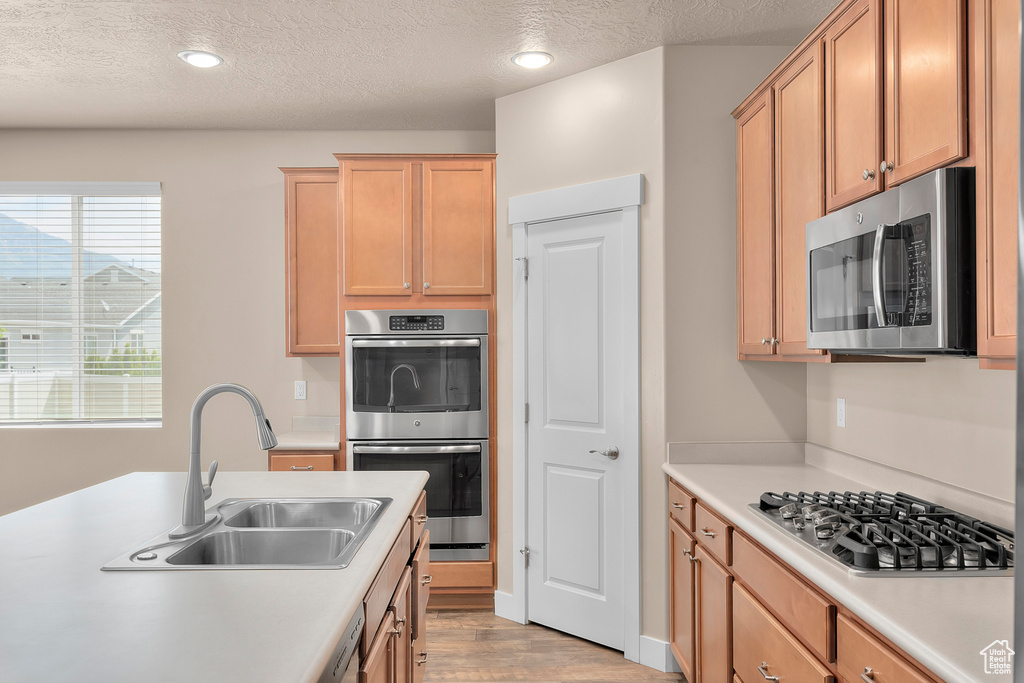 Kitchen featuring appliances with stainless steel finishes, sink, a textured ceiling, and light hardwood / wood-style flooring