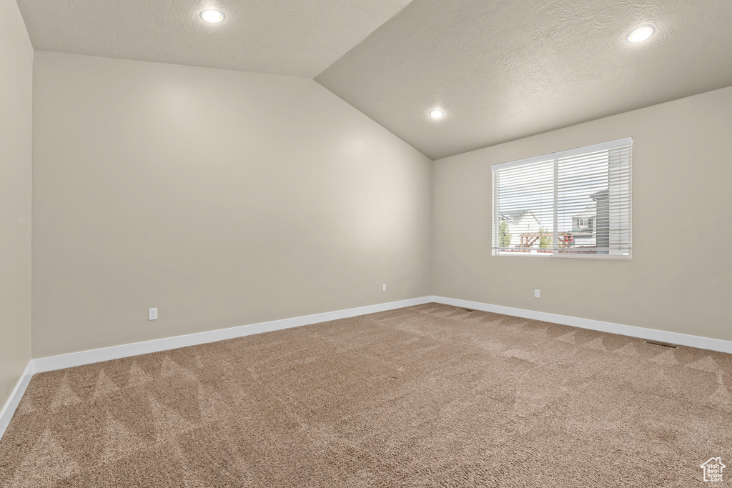 Unfurnished room featuring a textured ceiling, carpet, and vaulted ceiling