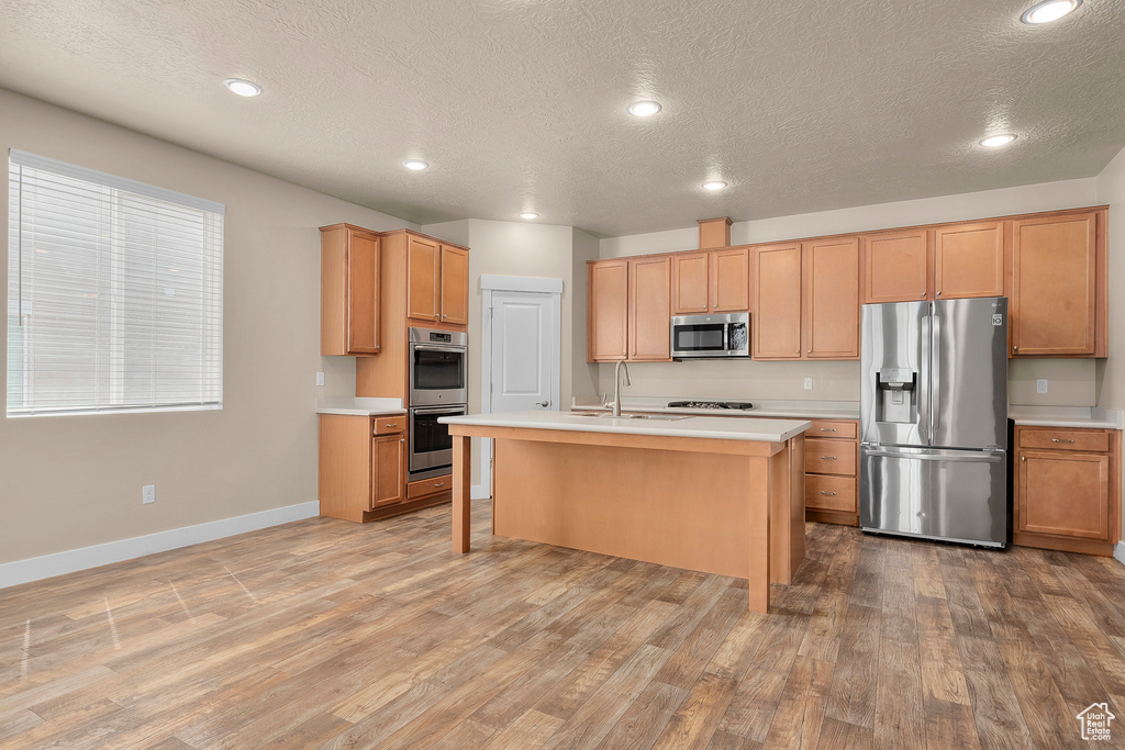 Kitchen with an island with sink, stainless steel appliances, wood-type flooring, a textured ceiling, and sink