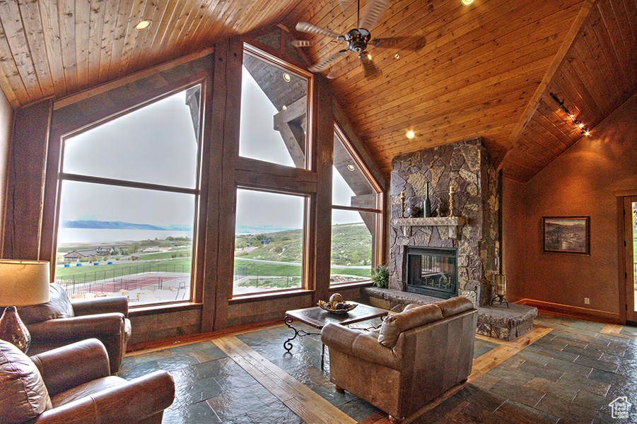 Tiled living room featuring high vaulted ceiling, a stone fireplace, ceiling fan, and wood ceiling