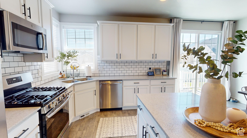 Kitchen featuring appliances with stainless steel finishes, light hardwood / wood-style floors, white cabinets, and tasteful backsplash