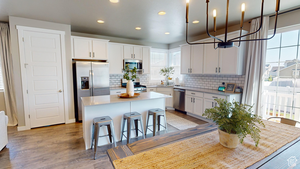 Kitchen with backsplash, a kitchen island, white cabinets, hardwood / wood-style flooring, and appliances with stainless steel finishes