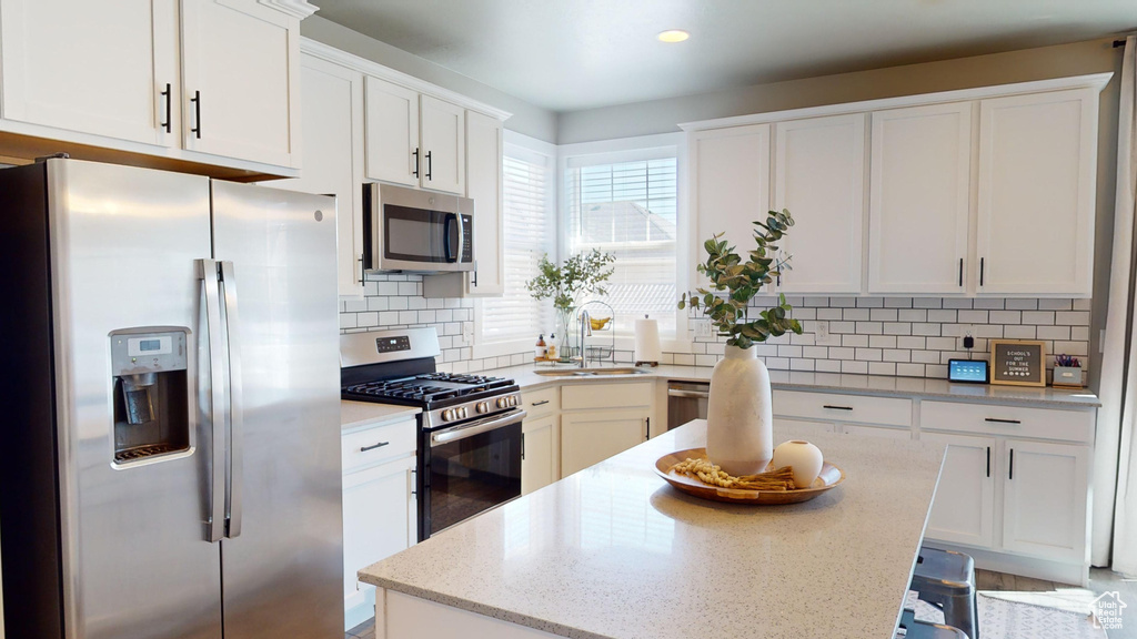 Kitchen featuring a center island, white cabinetry, backsplash, and stainless steel appliances