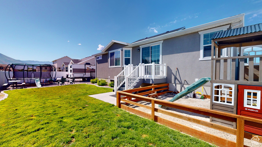 Back of property featuring a trampoline, a patio area, and a yard