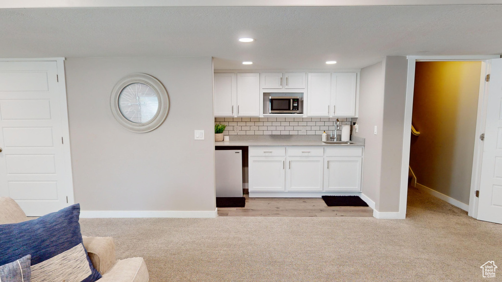 Kitchen featuring backsplash, white cabinets, dishwashing machine, and light hardwood / wood-style flooring