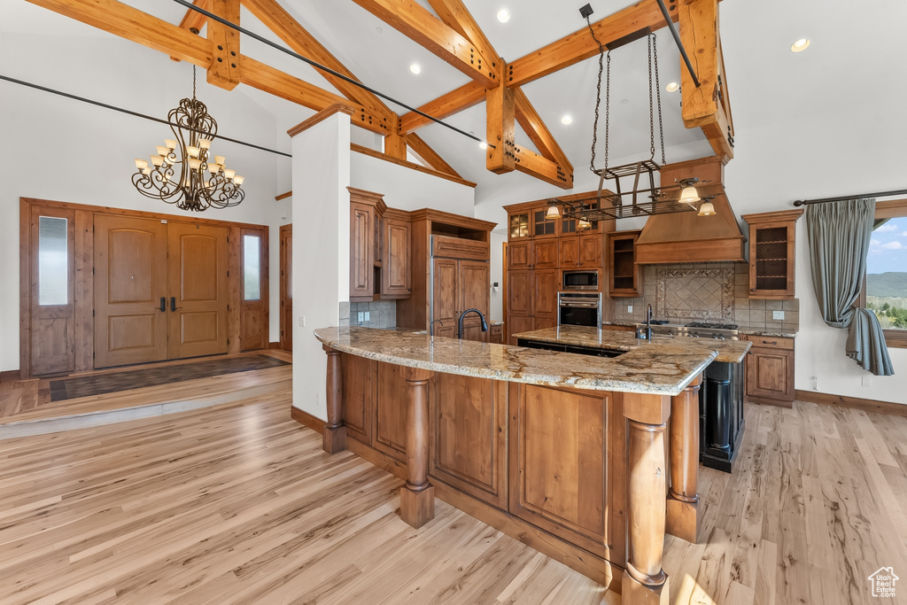 Kitchen with light hardwood / wood-style floors, light stone countertops, beamed ceiling, built in appliances, and backsplash