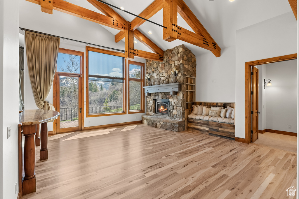 Unfurnished living room featuring high vaulted ceiling, beamed ceiling, a stone fireplace, and light hardwood / wood-style flooring