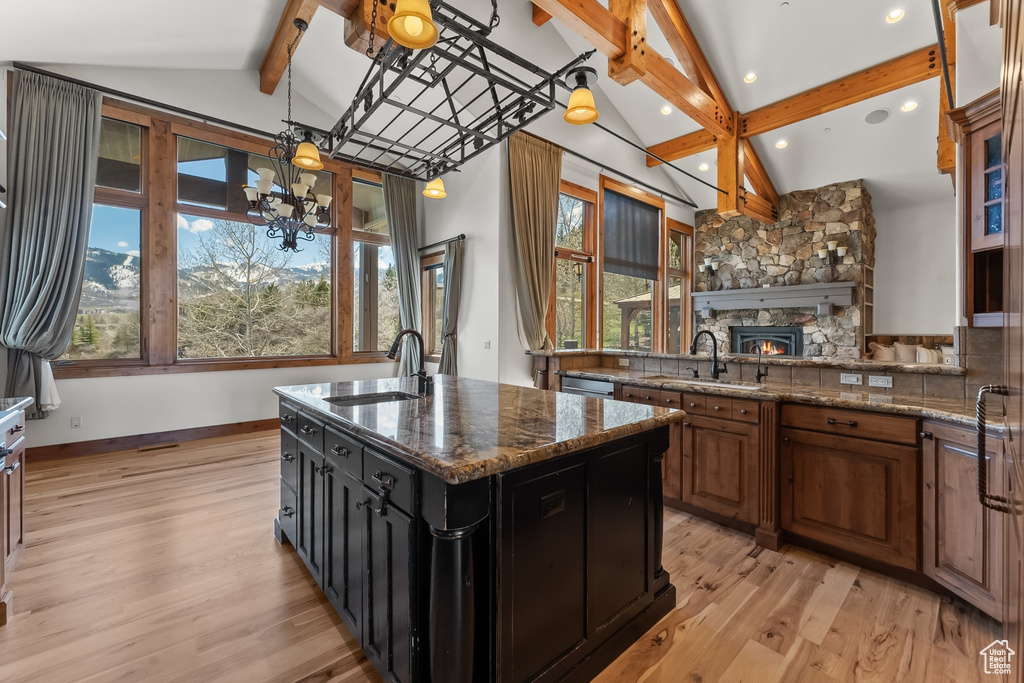 Kitchen featuring a fireplace, light wood-type flooring, a kitchen island with sink, beam ceiling, and sink