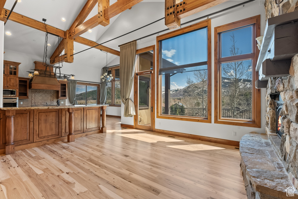 Living room featuring high vaulted ceiling, beamed ceiling, a stone fireplace, and light hardwood / wood-style flooring