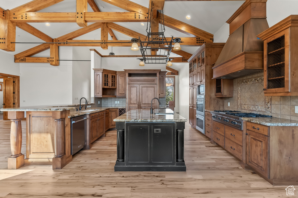 Kitchen with an island with sink, custom range hood, light hardwood / wood-style floors, and tasteful backsplash