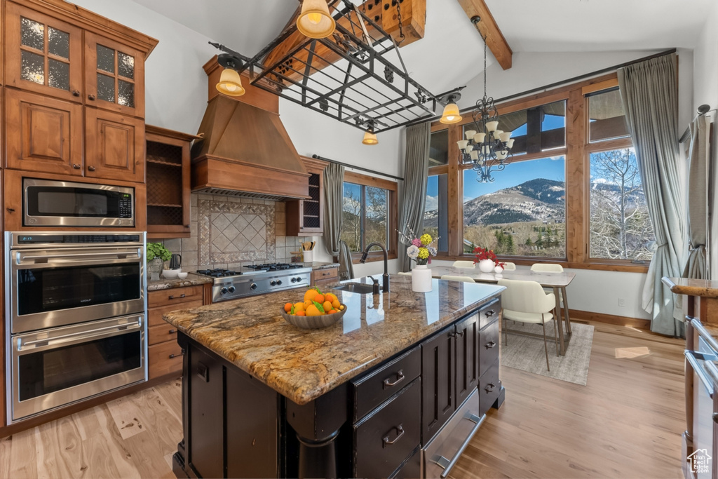 Kitchen with a chandelier, light hardwood / wood-style flooring, a center island with sink, a mountain view, and premium range hood