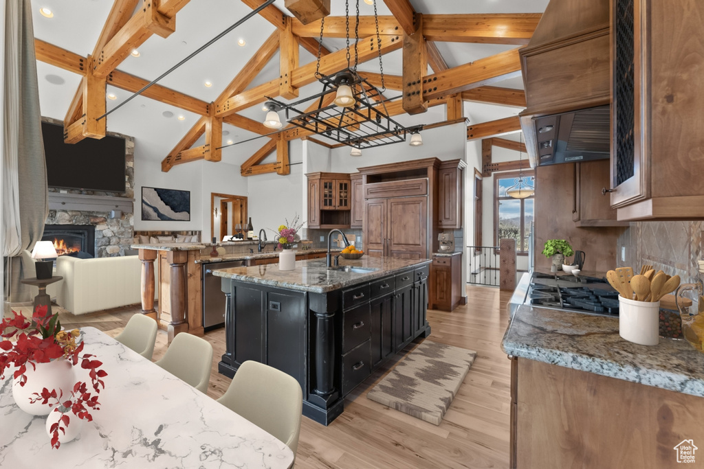 Kitchen with light wood-type flooring, a kitchen island with sink, a breakfast bar, a stone fireplace, and tasteful backsplash