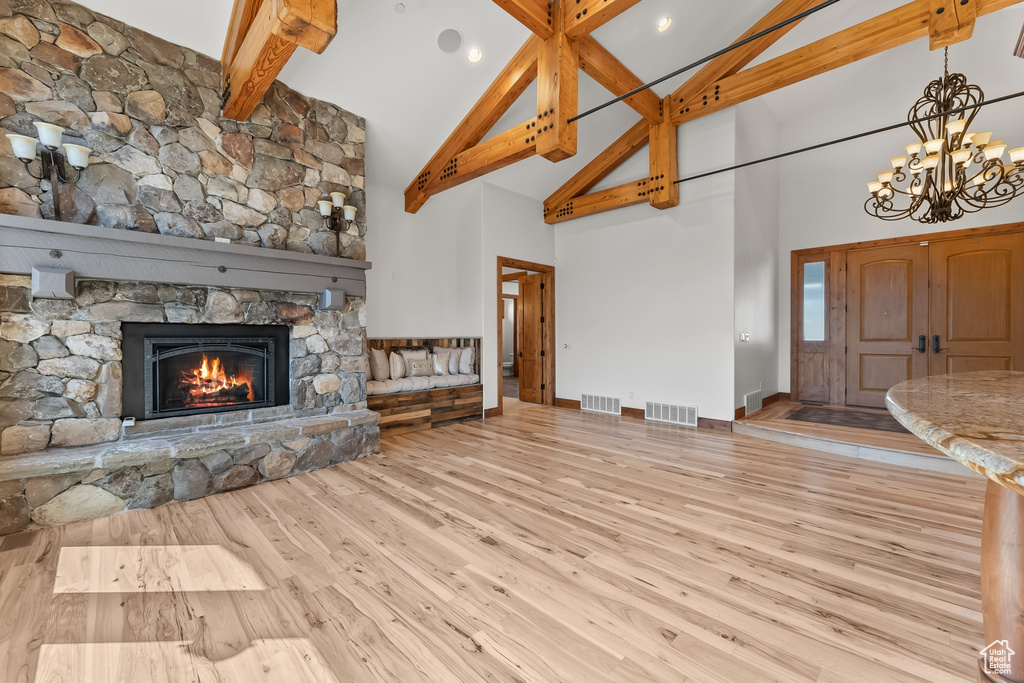 Unfurnished living room with a stone fireplace, light hardwood / wood-style floors, beam ceiling, high vaulted ceiling, and a chandelier