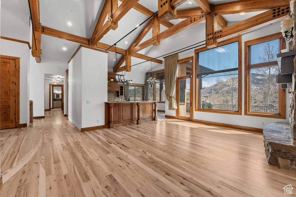 Unfurnished living room with plenty of natural light, beam ceiling, light wood-type flooring, and high vaulted ceiling