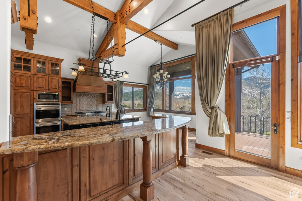 Kitchen with plenty of natural light, custom range hood, tasteful backsplash, and light hardwood / wood-style flooring