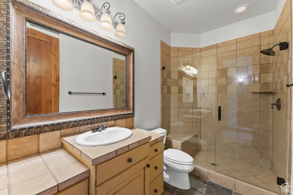 Bathroom with a shower with shower door, tile floors, toilet, and vanity with extensive cabinet space