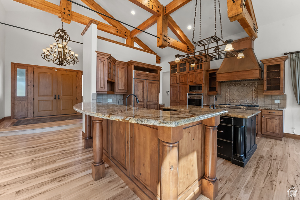 Kitchen with light stone countertops, a spacious island, light wood-type flooring, tasteful backsplash, and custom exhaust hood