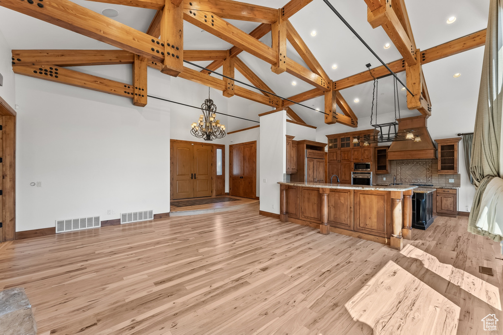 Kitchen featuring appliances with stainless steel finishes, high vaulted ceiling, backsplash, and light wood-type flooring