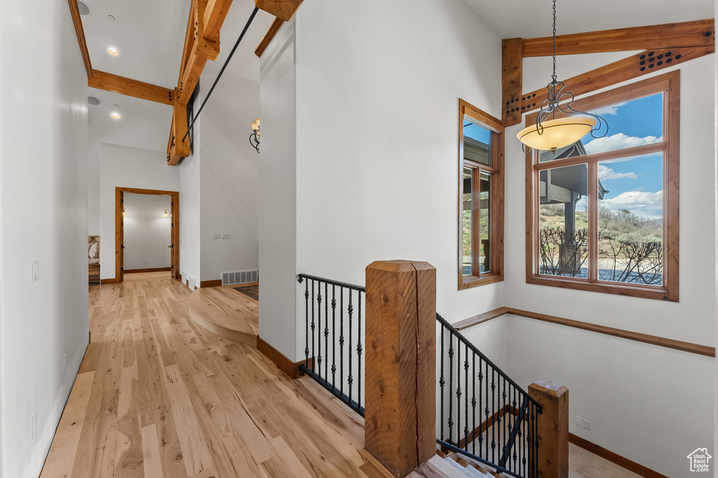 Hallway with beamed ceiling, a towering ceiling, and light wood-type flooring