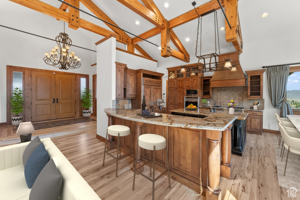 Kitchen with stainless steel appliances, beam ceiling, light wood-type flooring, backsplash, and hanging light fixtures