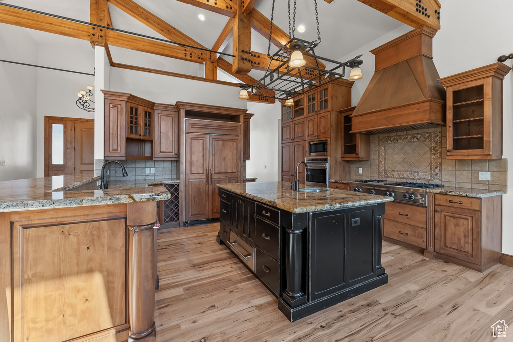 Kitchen featuring light hardwood / wood-style flooring, built in appliances, premium range hood, light stone counters, and a kitchen island