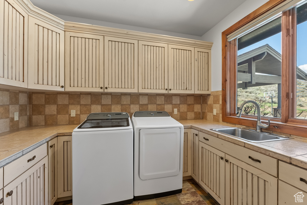 Clothes washing area with tile flooring, sink, washer and dryer, and cabinets