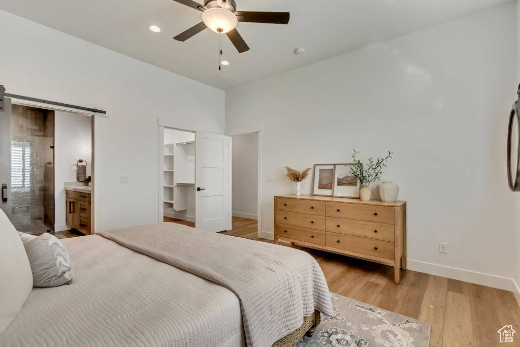 Bedroom featuring a barn door, ensuite bathroom, ceiling fan, light hardwood / wood-style flooring, and a walk in closet
